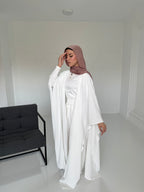 Person wearing a white outfit and brown hijab in a minimalistic room with a black sofa.