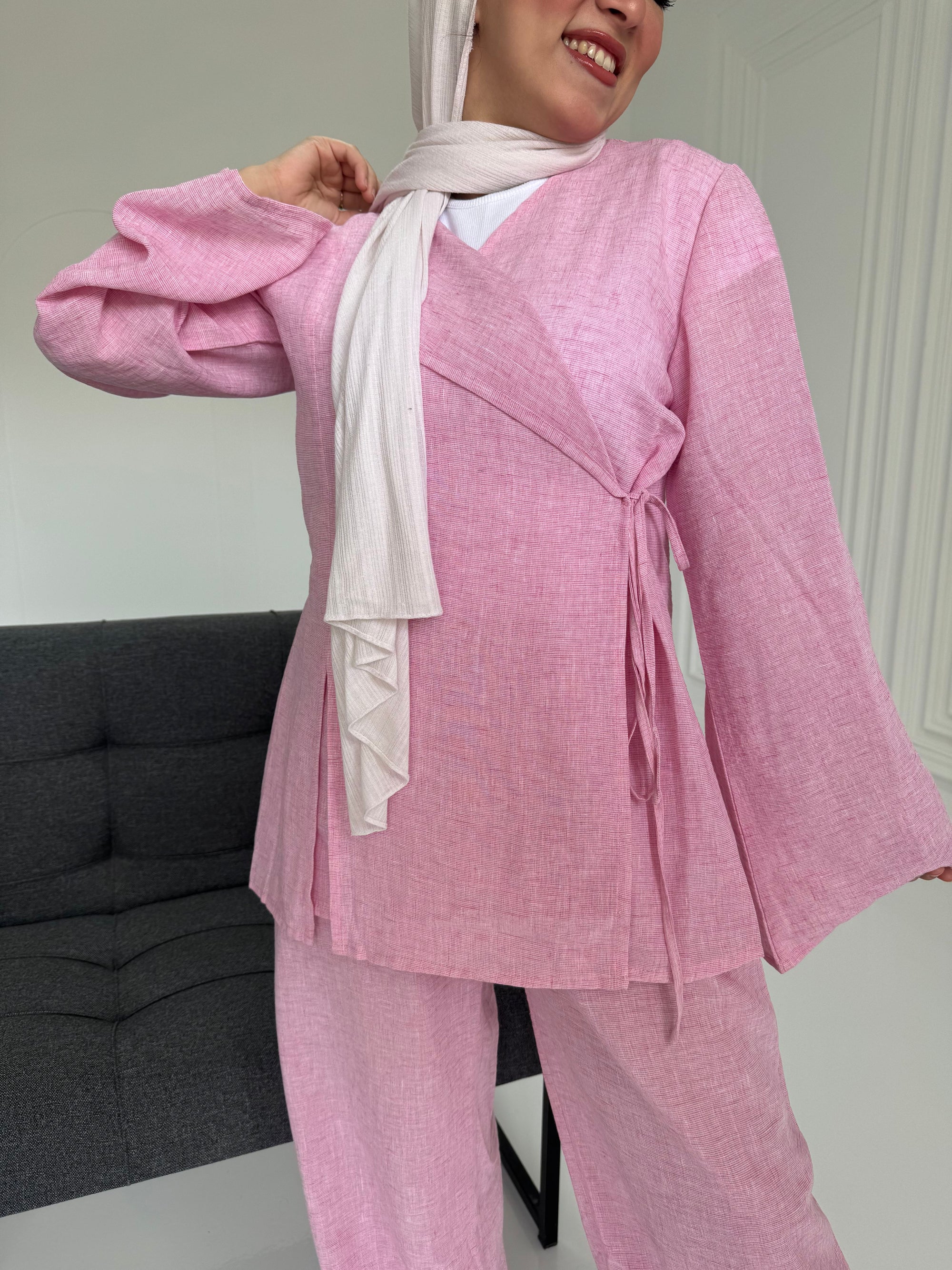 Woman wearing a pink outfit with a white scarf in a room.