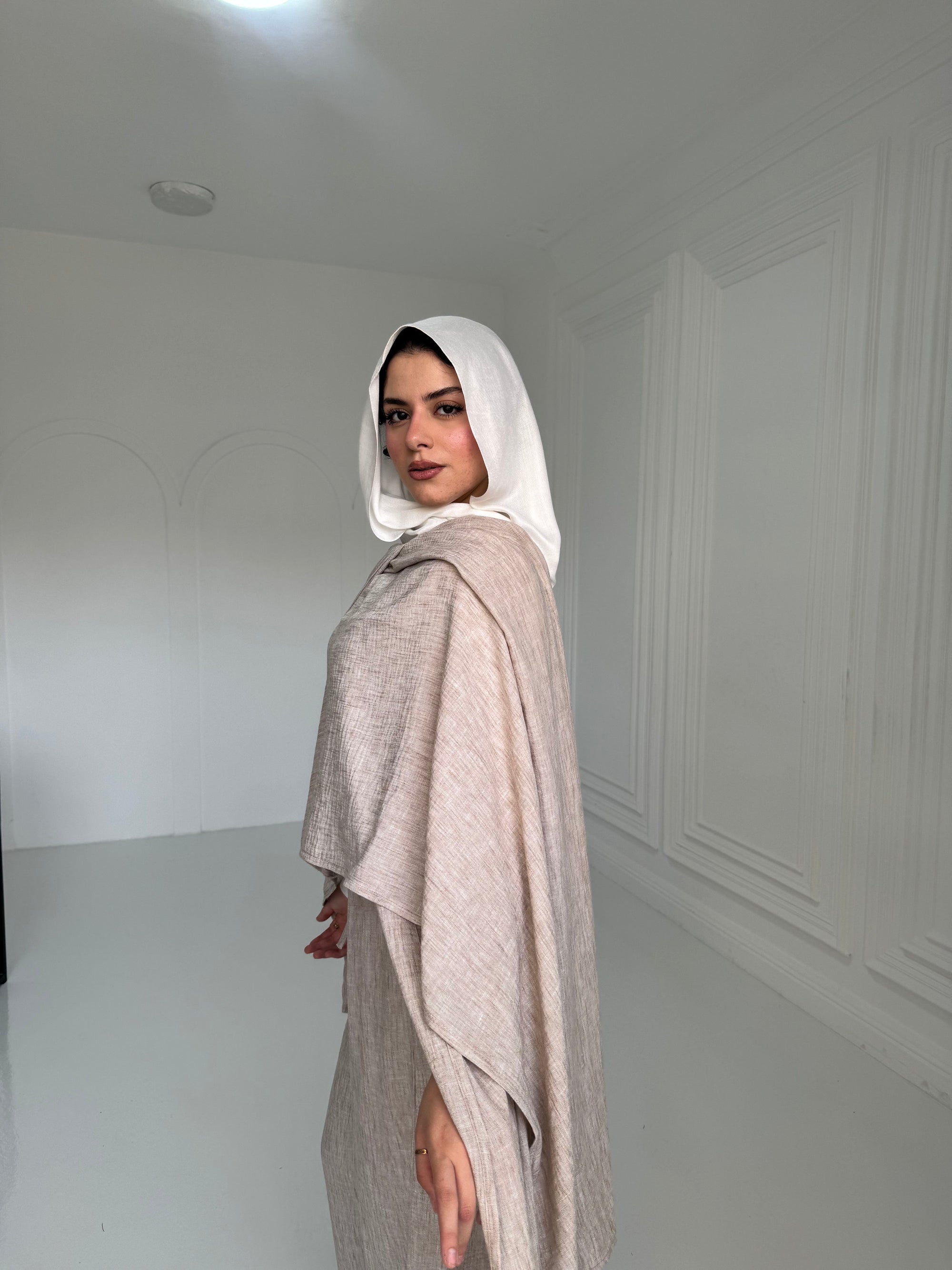 Woman wearing a white hijab and beige outfit in a minimalistic room.