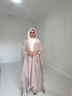 Woman wearing a beige abaya and white hijab in a white room