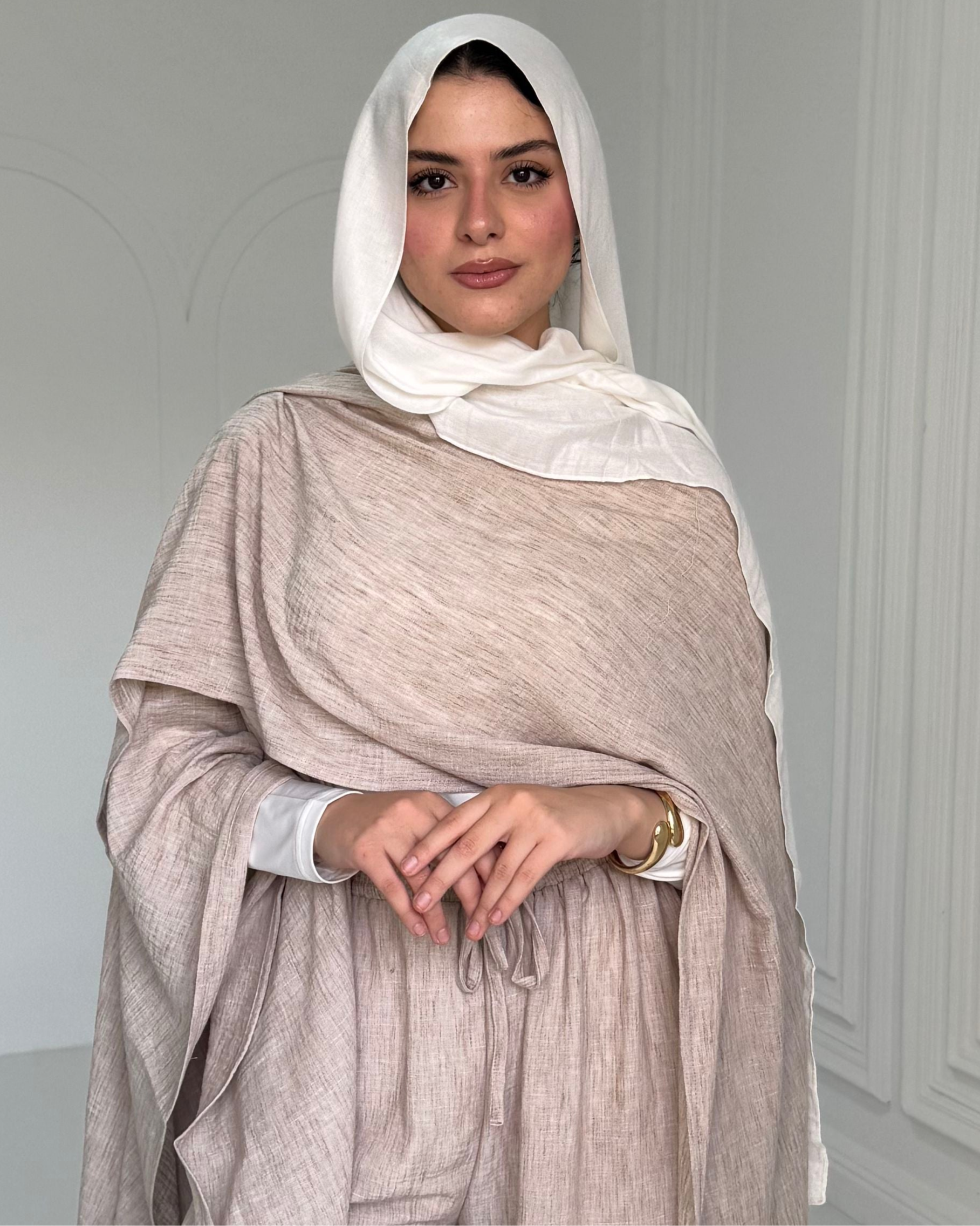 Woman wearing a beige shawl and white hijab against a light gray background
