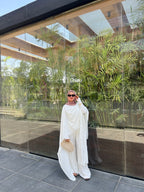 Woman in a white outfit standing in front of a glass wall with greenery.