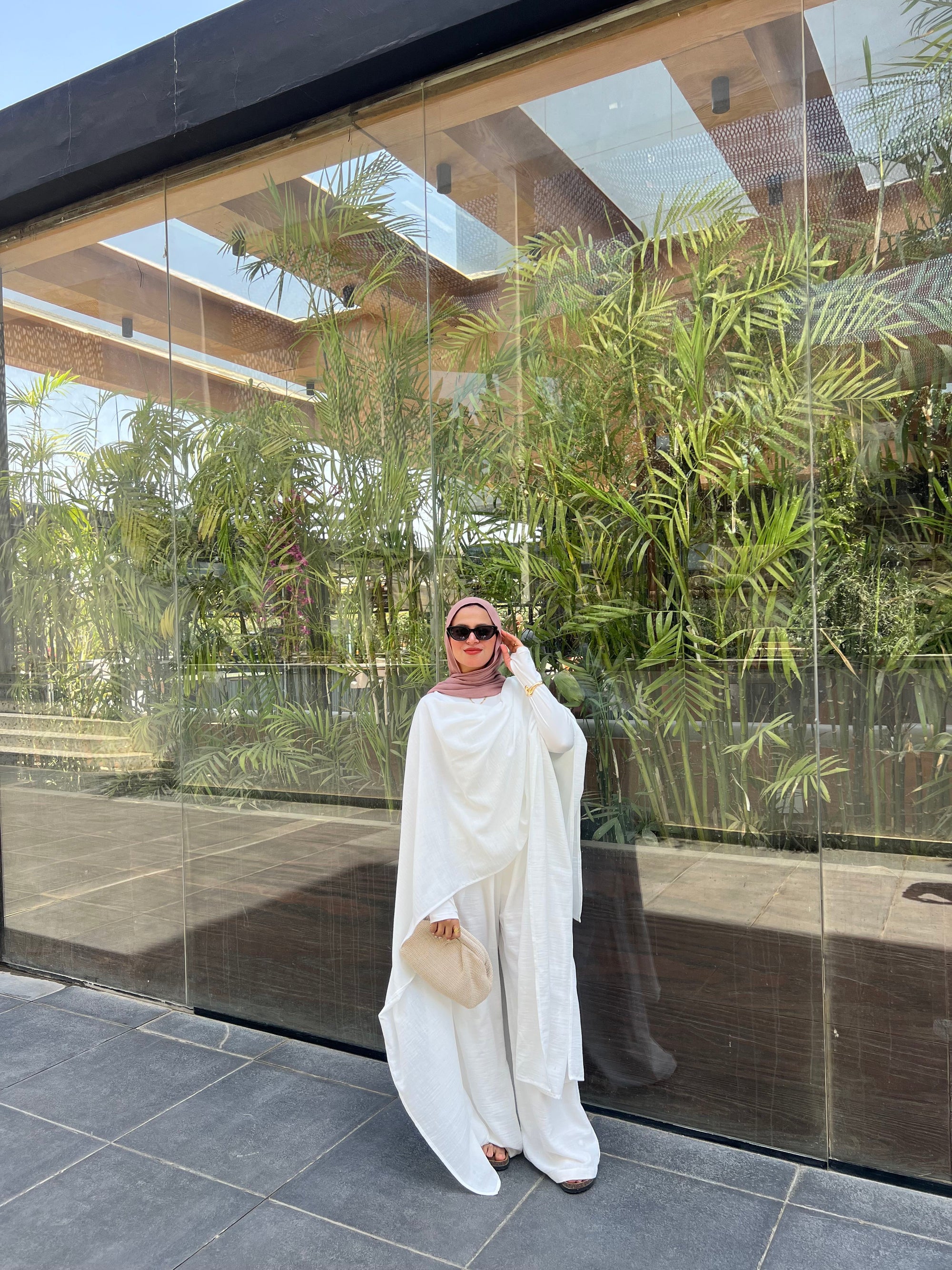 Woman in a white outfit standing in front of a glass wall with greenery.