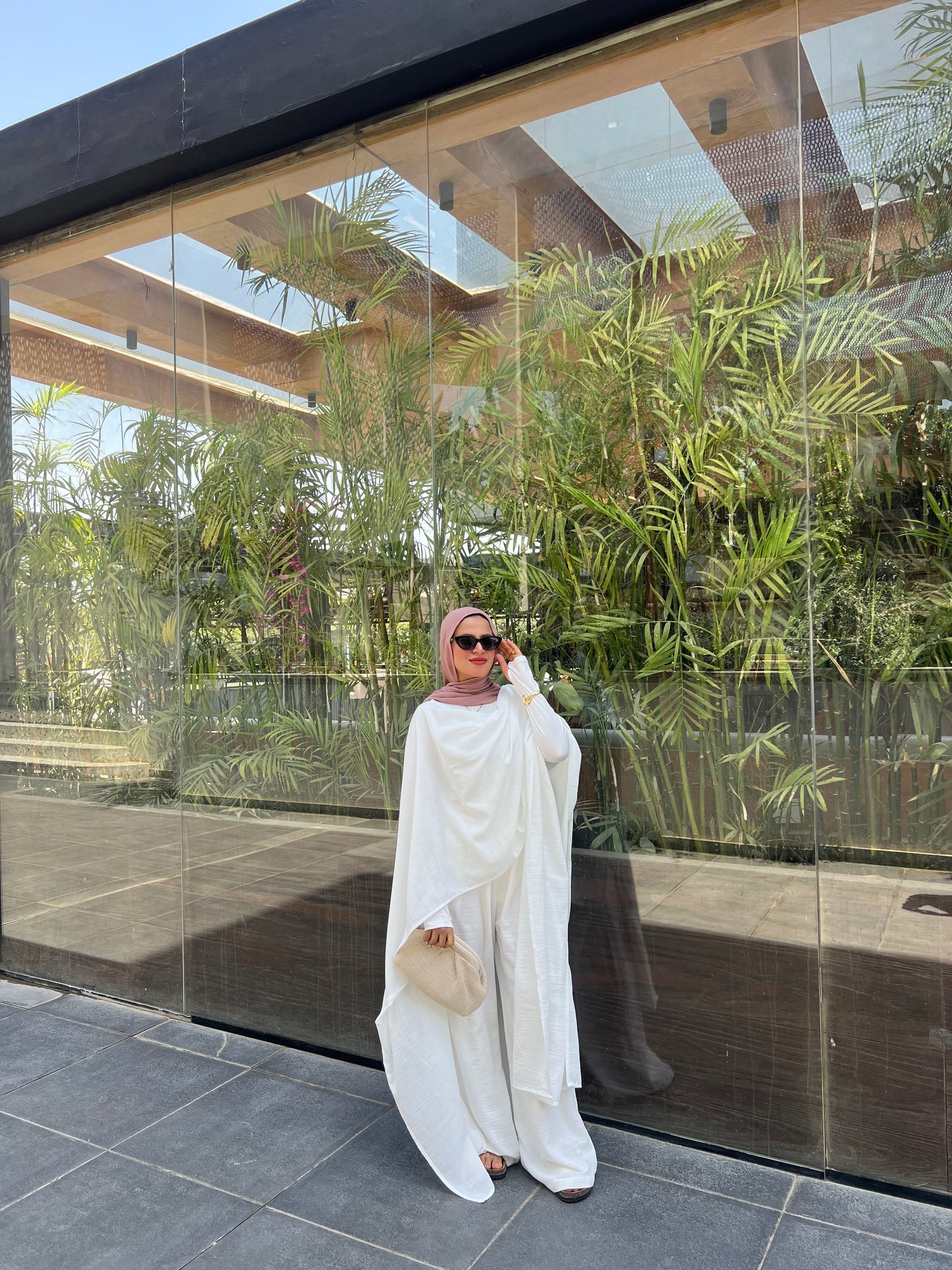 Woman in a white outfit standing in front of a glass wall with greenery outside.