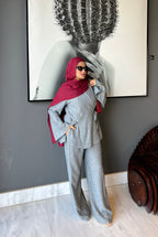 Woman in gray outfit and red hijab standing in front of a wall with a large framed picture.