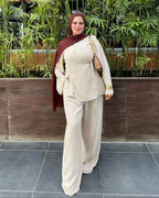 Woman in a beige outfit standing in front of a green plant wall.