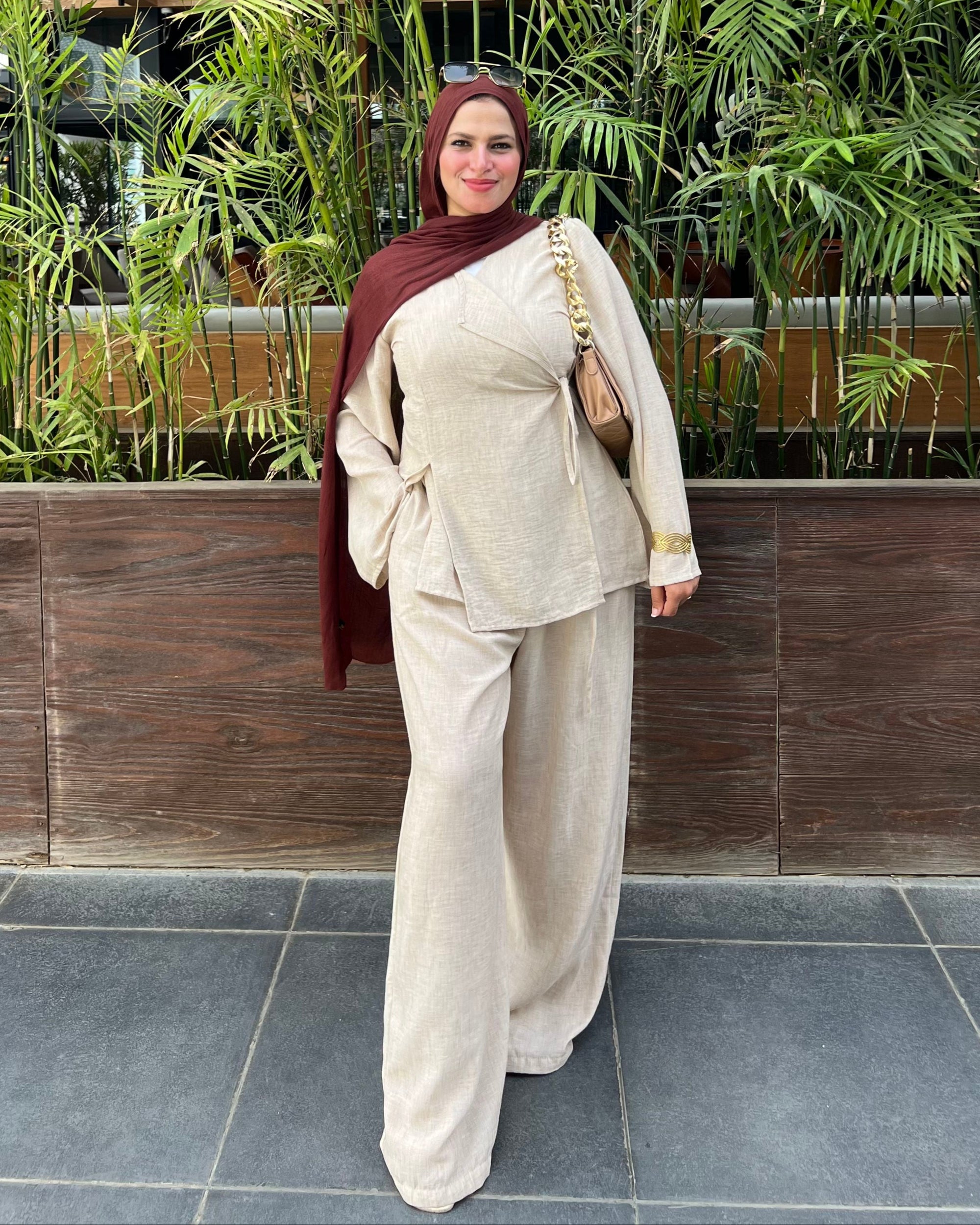 Woman in a beige outfit standing in front of a green plant wall.