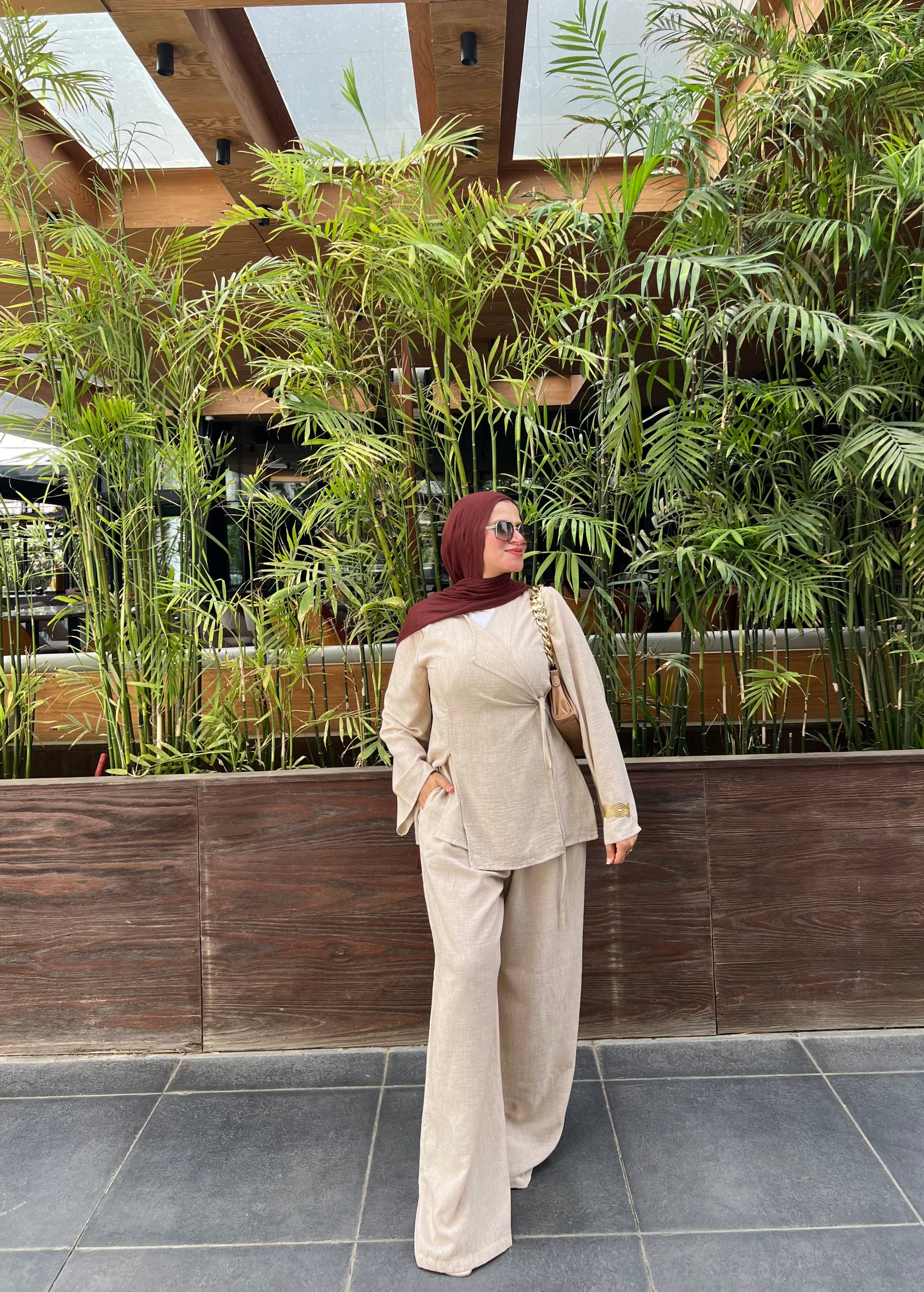 Woman in beige outfit standing in front of a green plant wall.