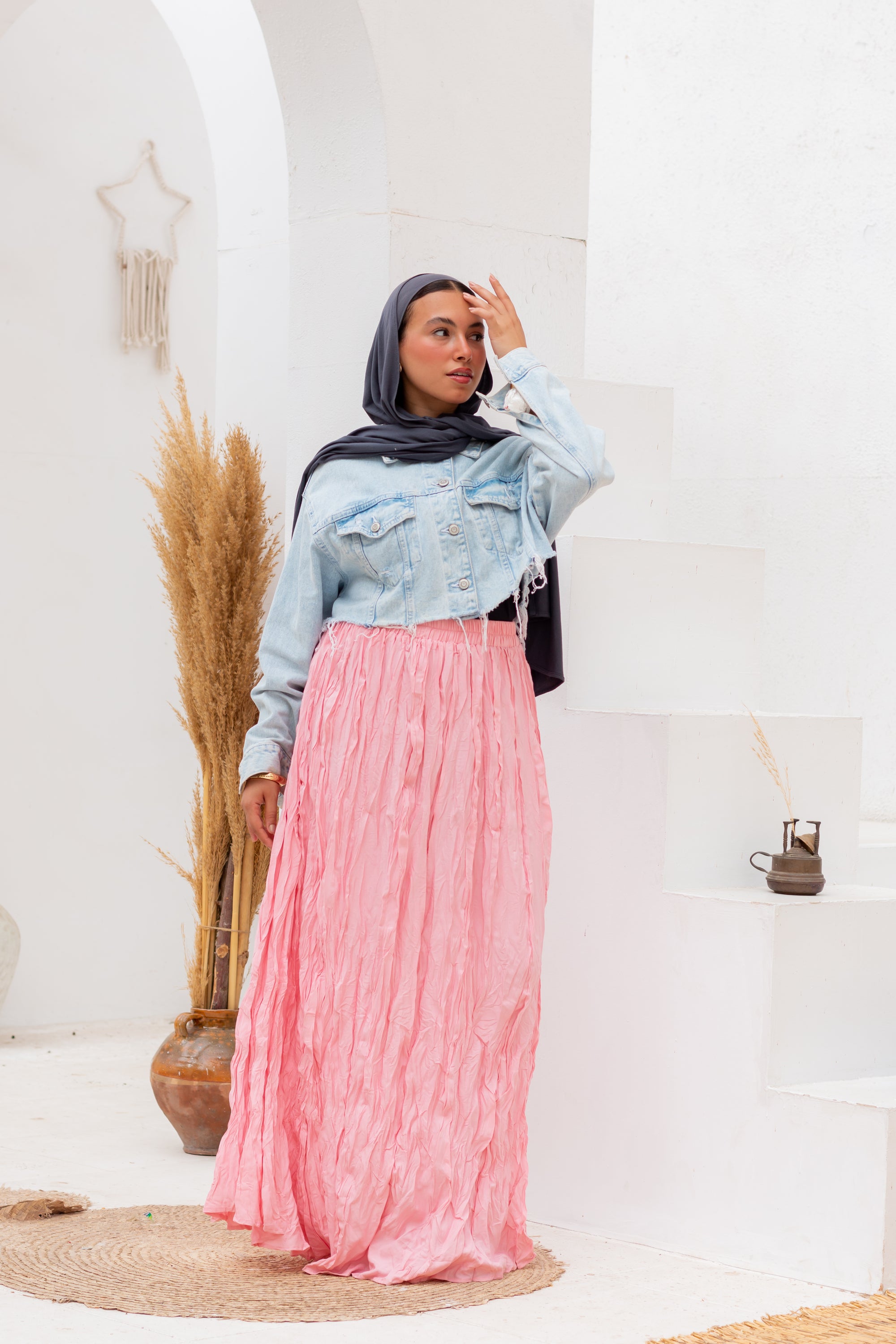 Woman wearing a light blue denim jacket and pink skirt indoors with decorative elements.