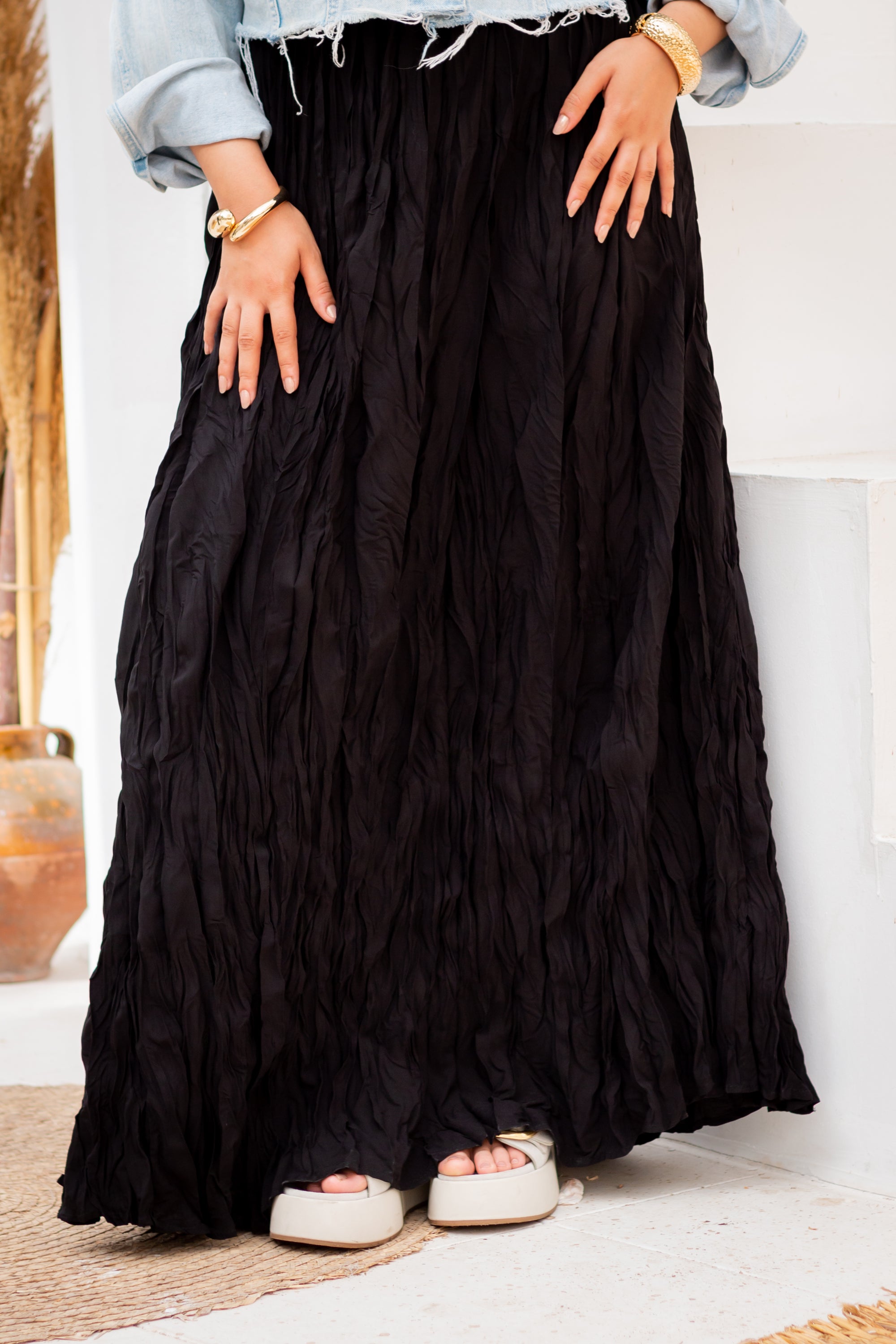 Person wearing a long black skirt with hands on hips against a white wall.