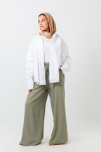 Woman wearing a white shirt, beige hijab, and green pants on a white background