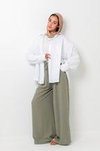 Woman wearing a white shirt and beige hijab with wide-leg green pants on a white background