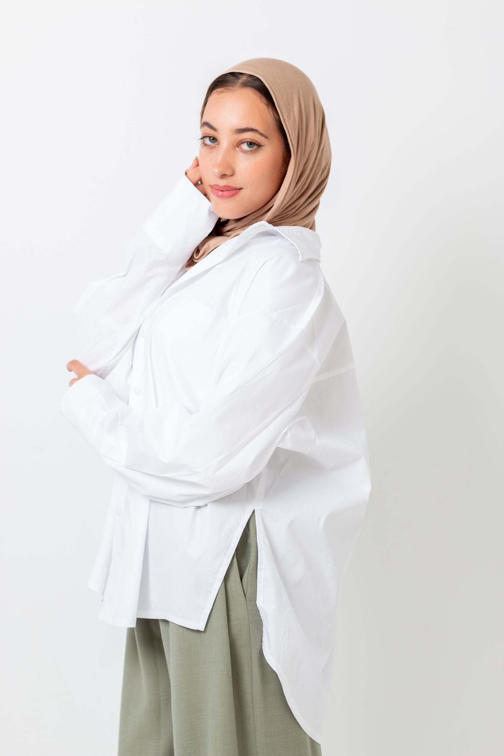 Woman wearing a beige hijab and white shirt with a light background