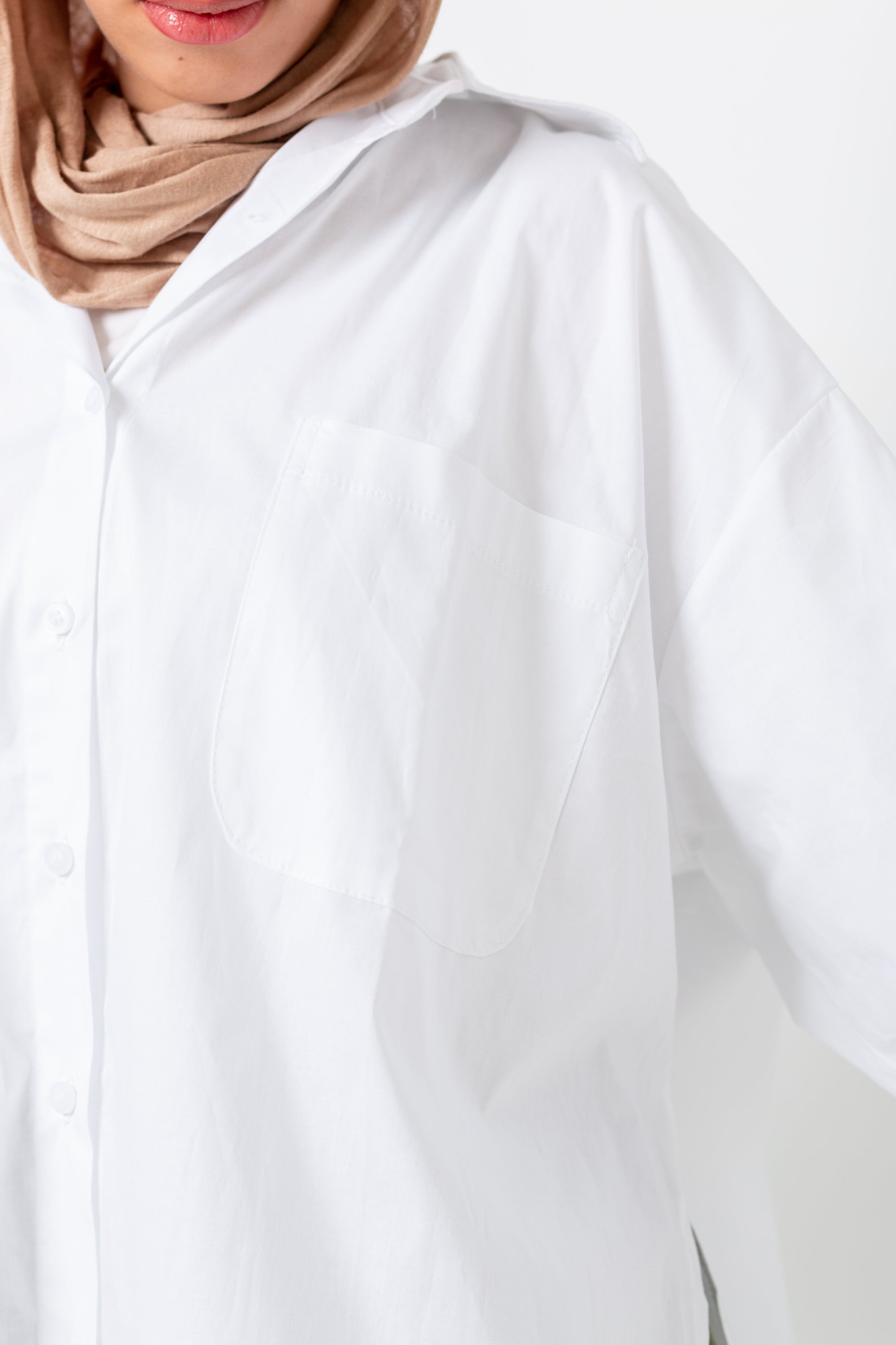 White abaya worn by a person with a beige hijab on a white background
