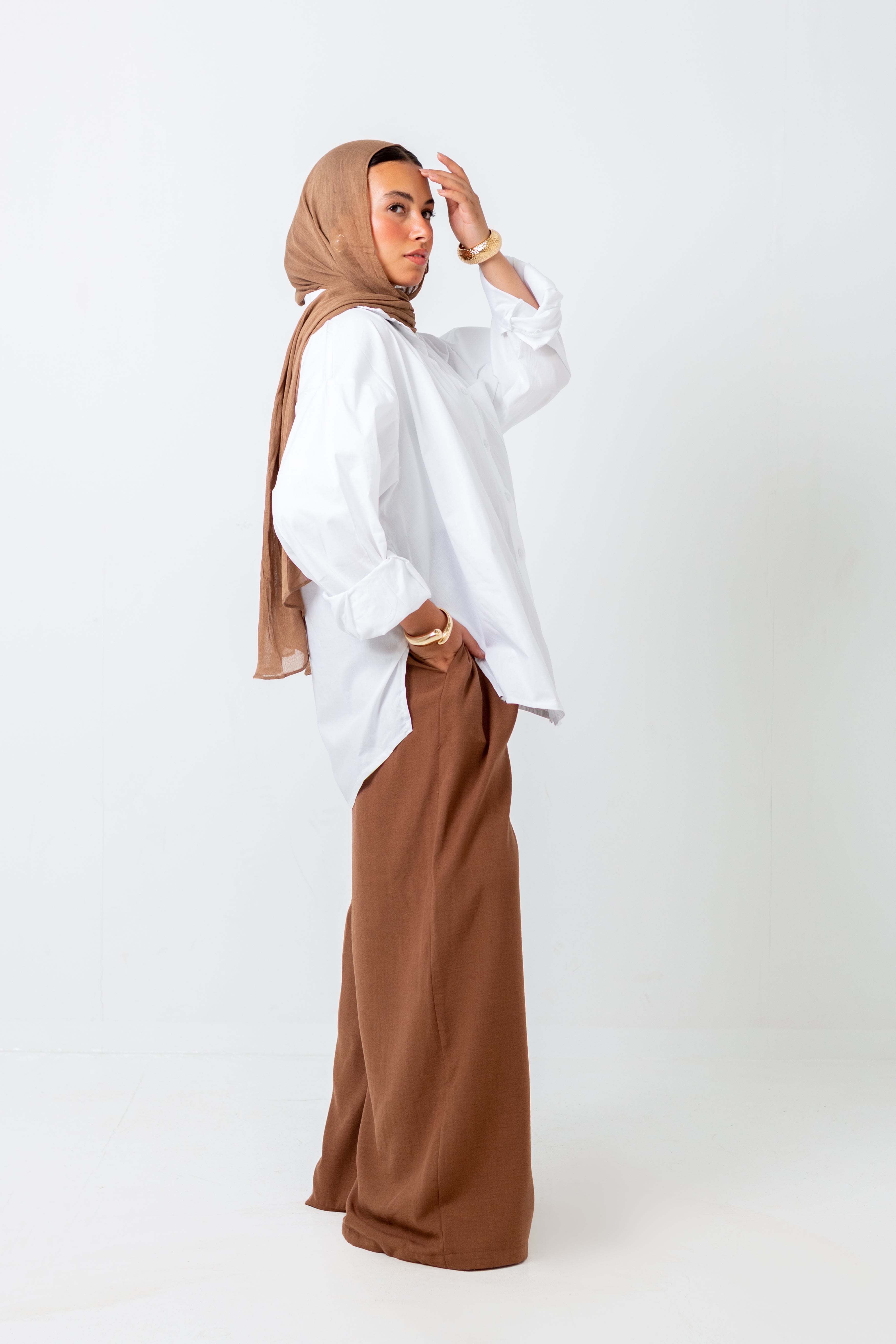 Woman wearing a white shirt and brown hijab and pants on a white background