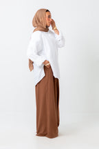 Woman wearing a white top and brown hijab and pants on a white background