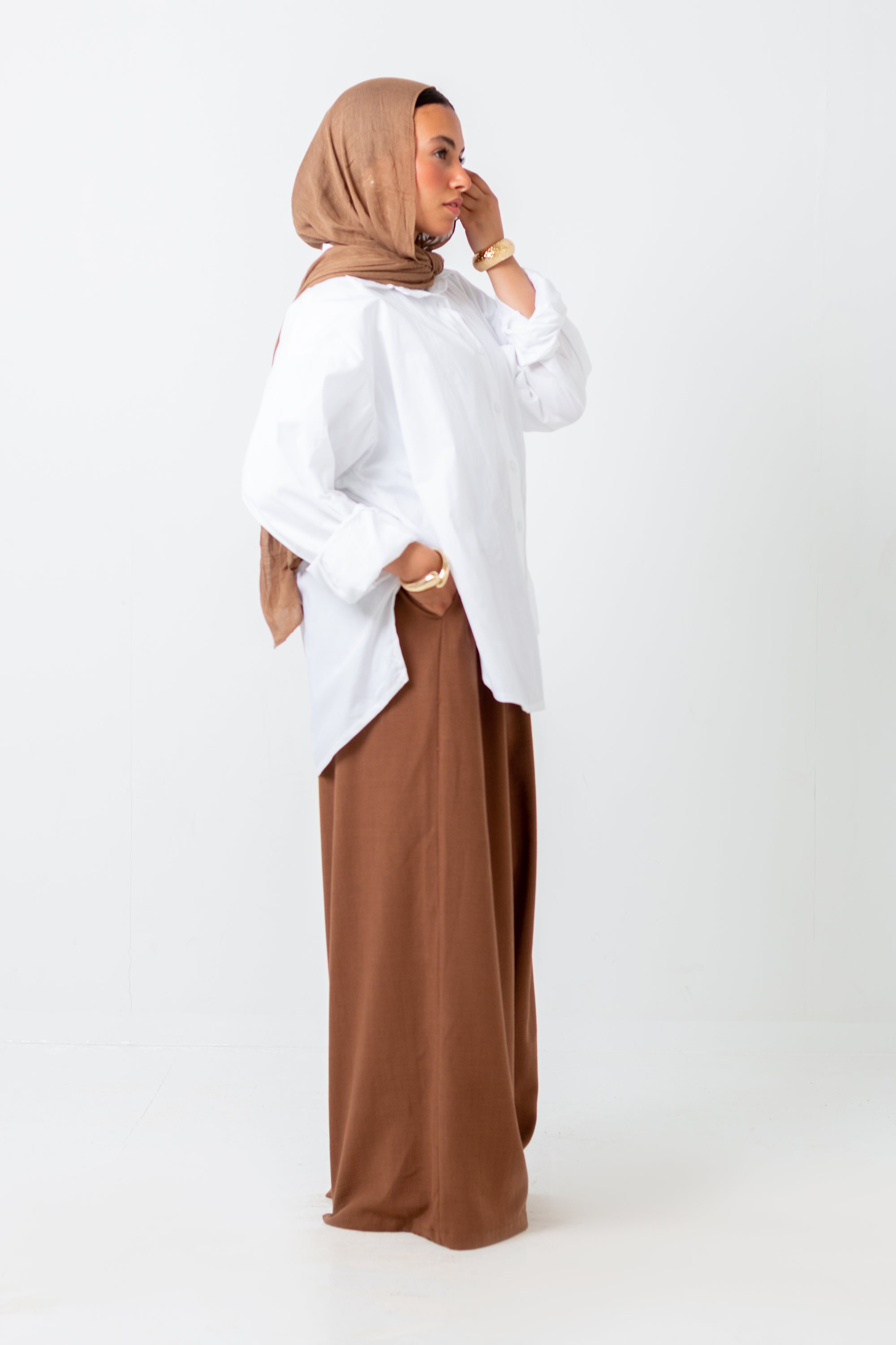 Woman wearing a white top and brown hijab and pants on a white background