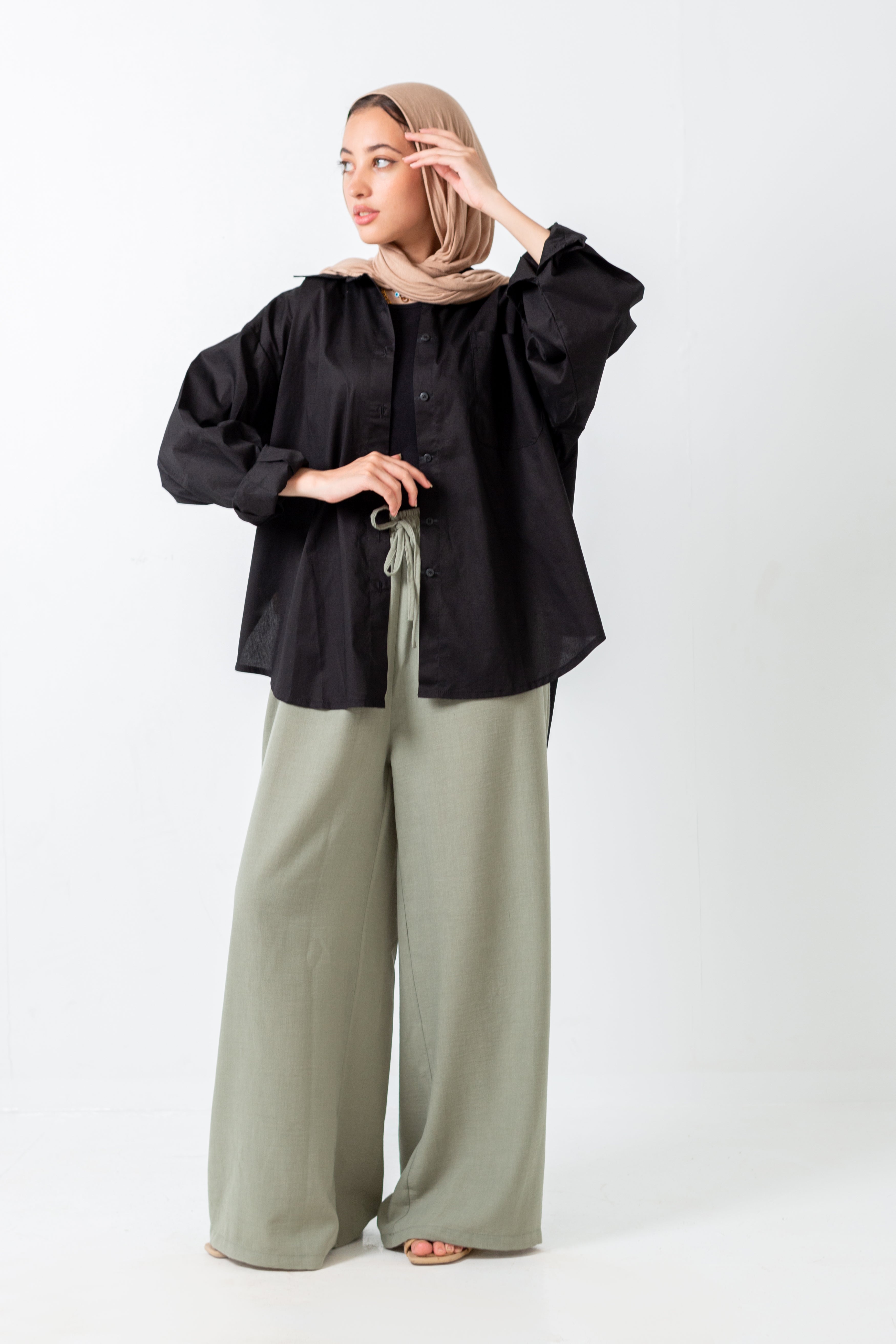 Woman wearing a black blouse and light green pants on a white background
