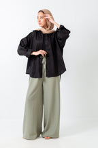 Woman wearing a black blouse and light green pants on a white background