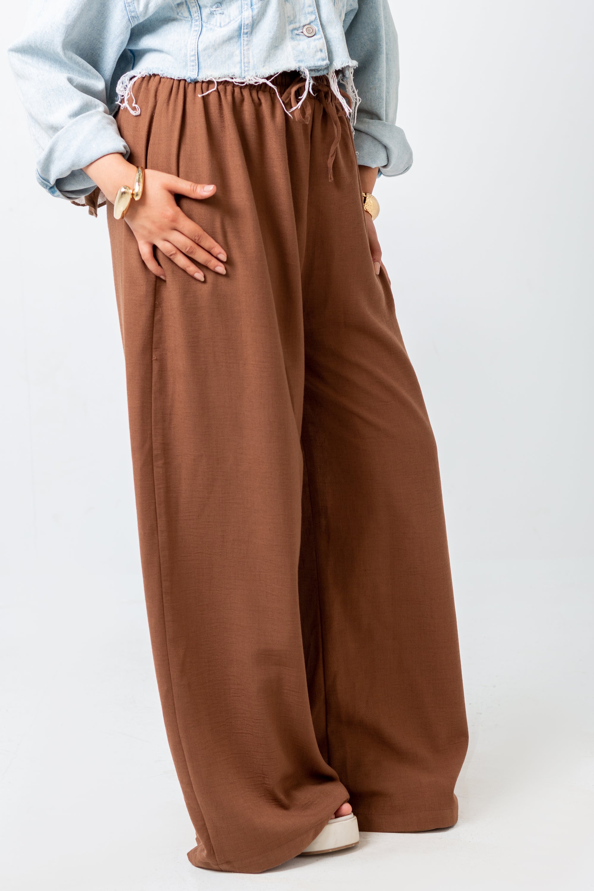 Person wearing brown wide-leg pants with a light blue denim jacket on a white background