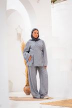 Woman wearing a gray outfit with a hijab standing in a white architectural setting.