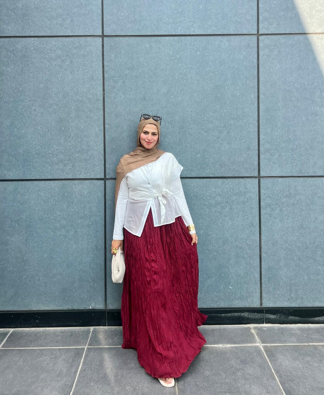 Woman in a white top and red skirt standing against a blue tiled wall.