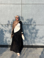 Woman in a black and white outfit with a headscarf standing against a gray wall.