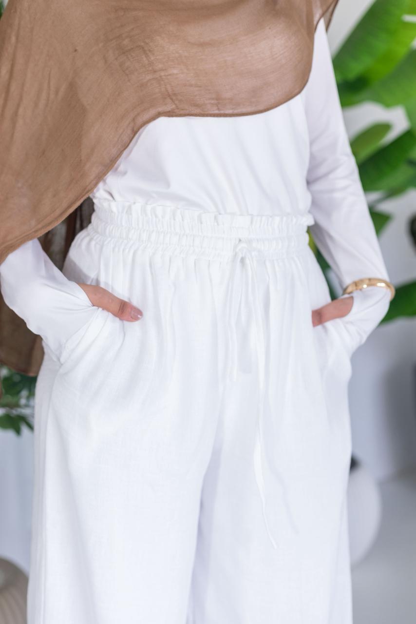 Person wearing a white outfit with a brown top against a blurred green background