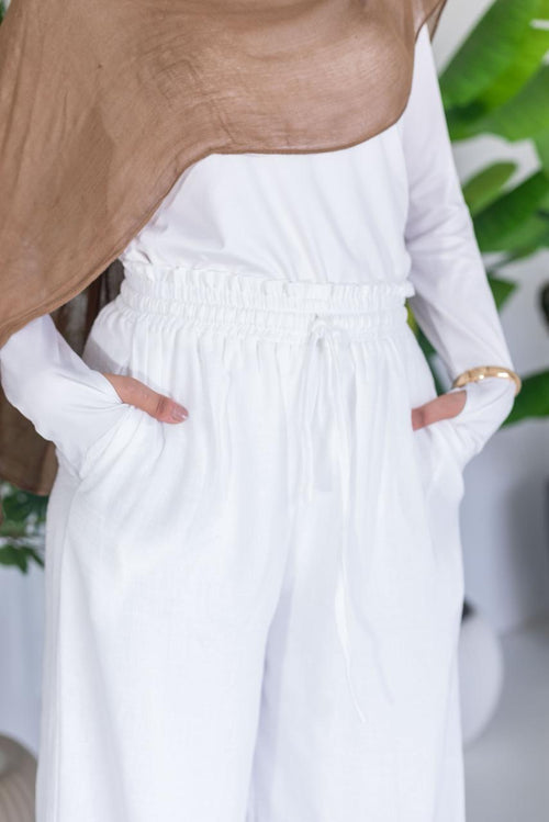 Person wearing a white outfit with a brown top against a blurred green background