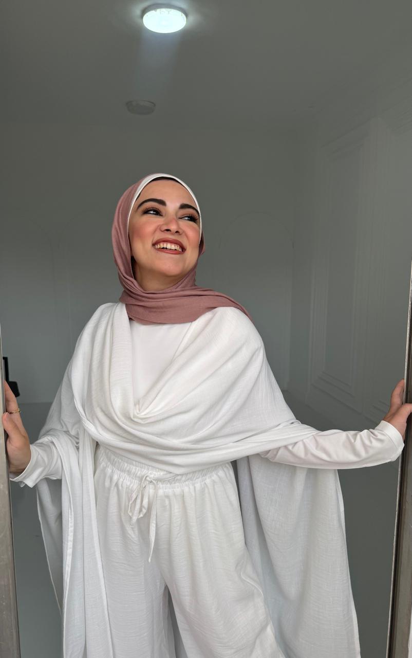 Woman wearing a white outfit with a pink hijab in a room.